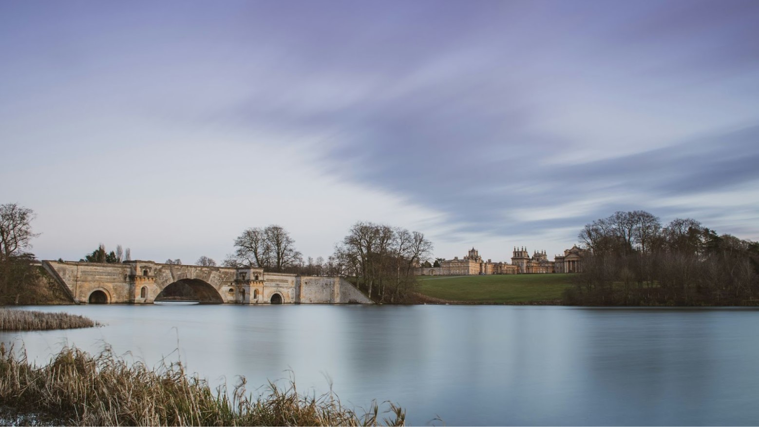 A body of water in Oxfordshire, England with an old bridge and grand castle in the distance.