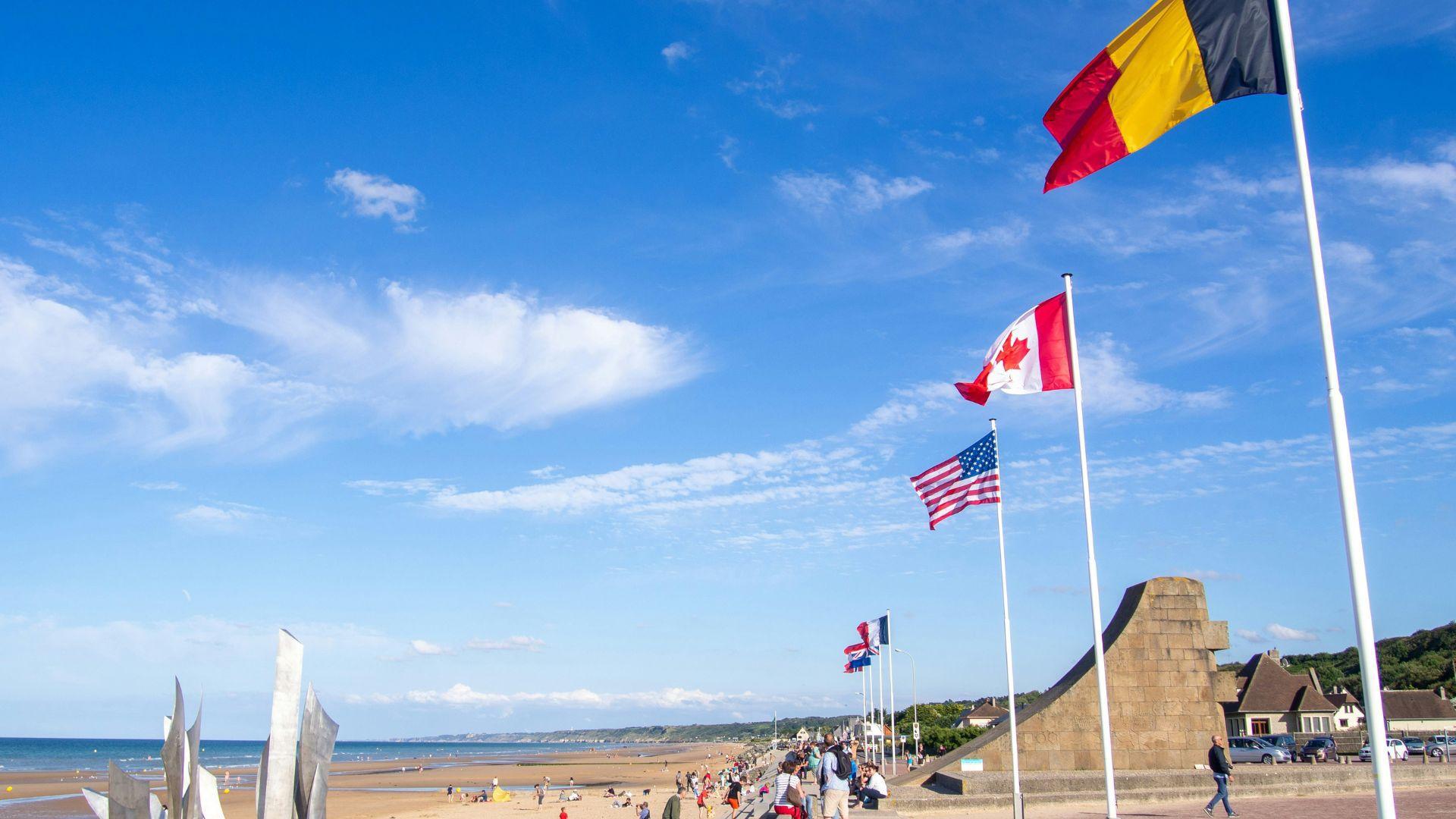 Various flags, including the American flag, seen on poles at the D-Day beach in France.