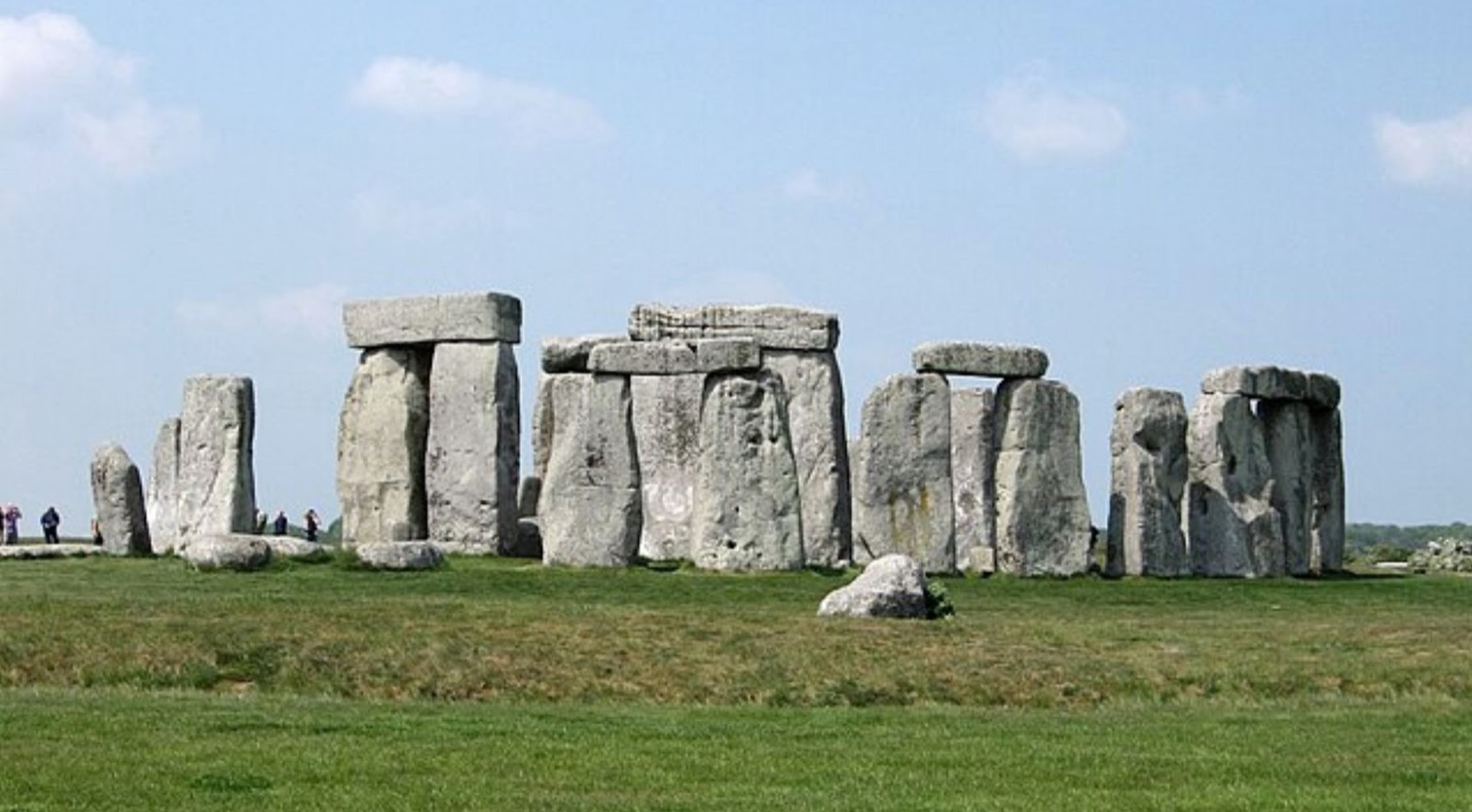 Stonehenge on a sunny day. There are some people in the background looking at the stones.
