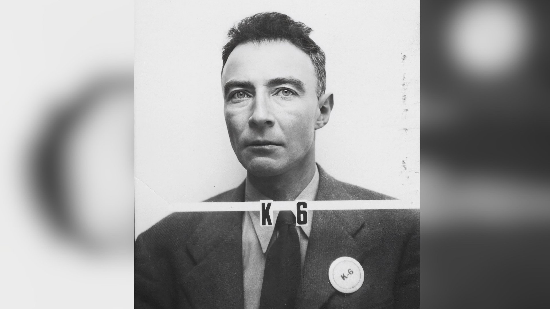 Black-and-white portrait photo of Robert Oppenheimer wearing his Los Alamos badge and a suit in the 1940s.