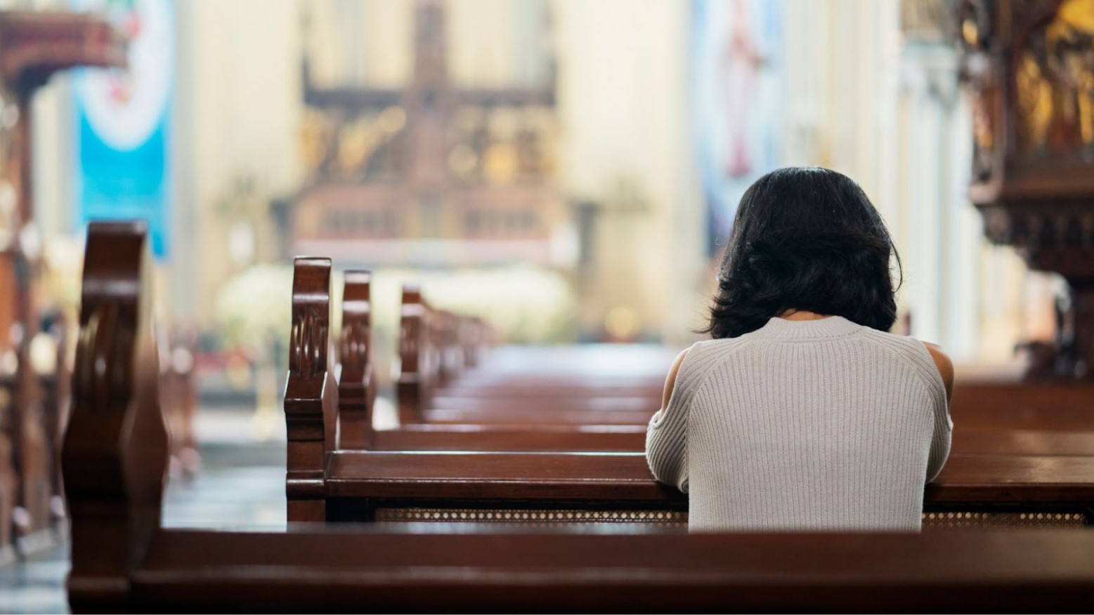 The back of a woman is shown sitting in a pew while praying at Church