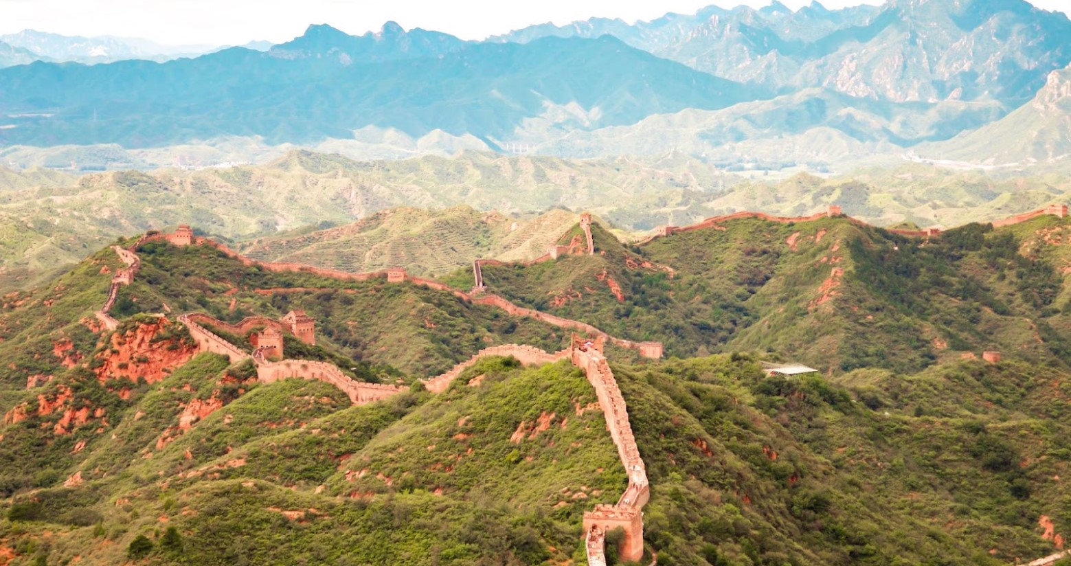 An aerial view of the Great Wall of China. The wall can be seen from towards the bottom of a hill and going up and around.
