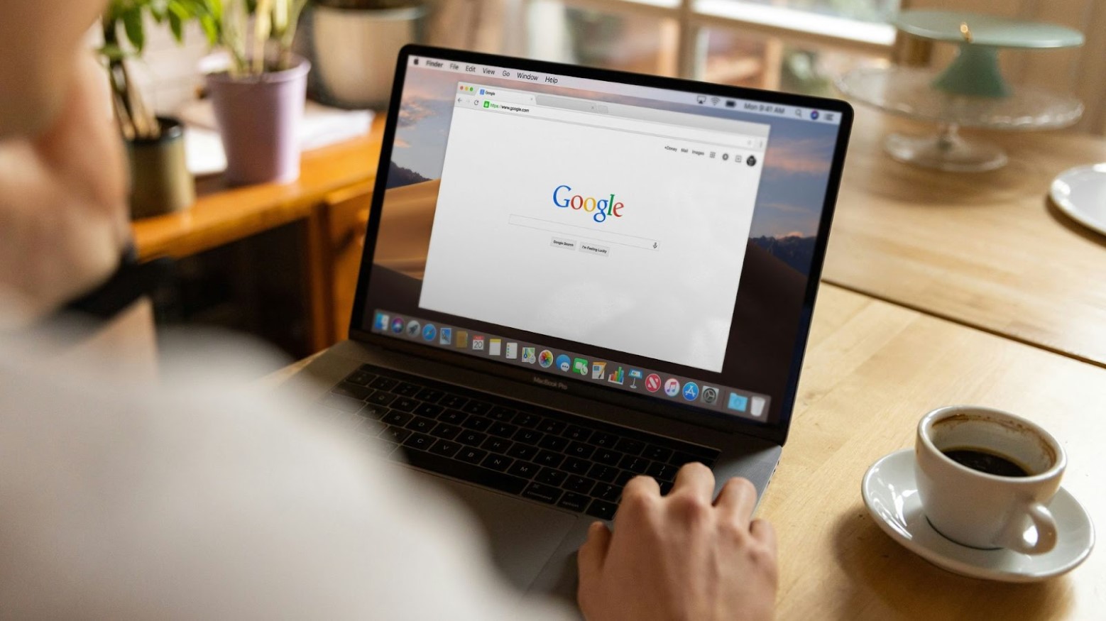 A person using their laptop, which is open to Google, with a mug and saucer on the surface beside them.