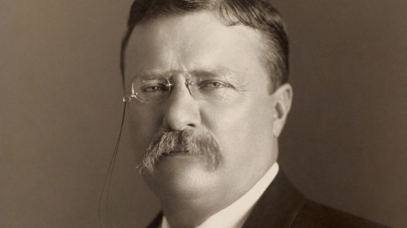 A sepia photo of Teddy Roosevelt wearing glasses.