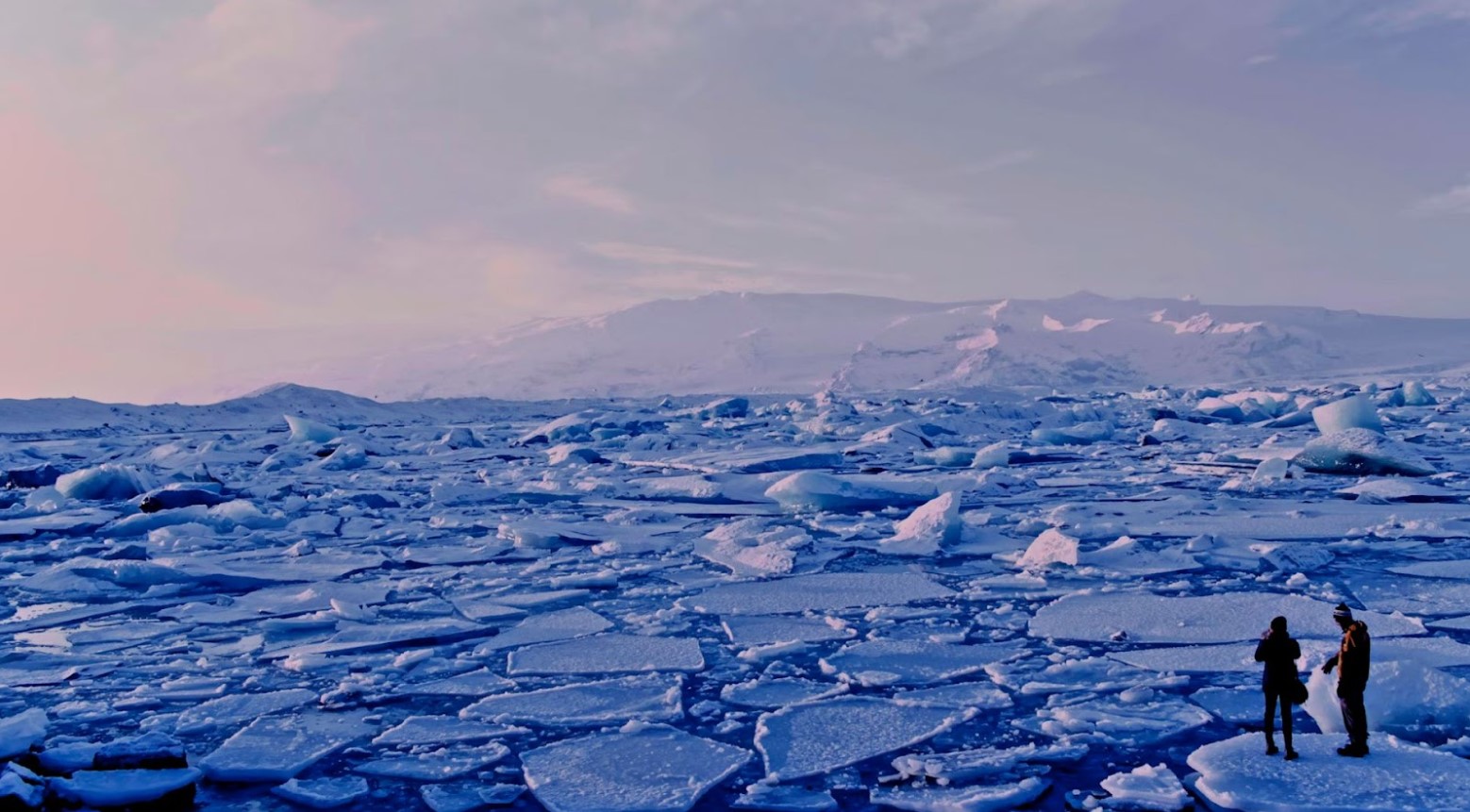 An example of global warming. Two people are standing on a block of ice. The rest of the ice has been broken up, with the water visible.