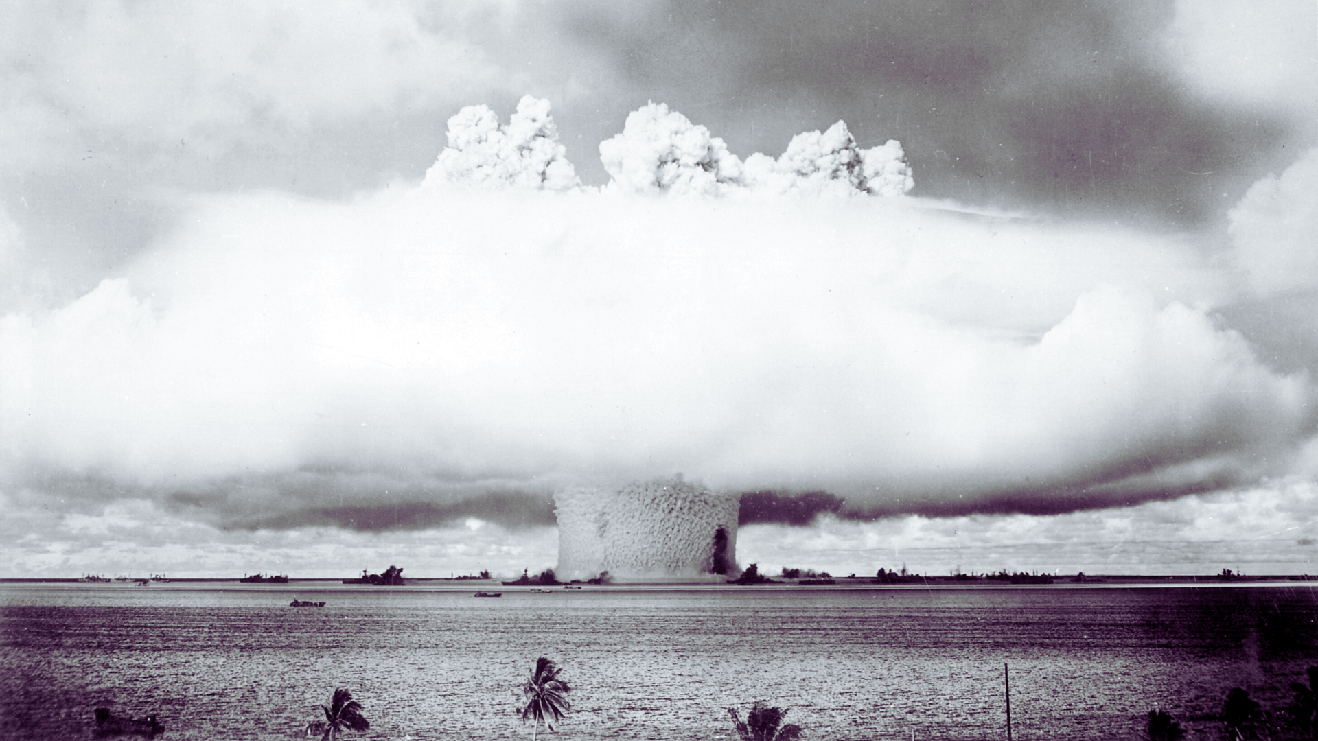 Black-and-white photo of the atomic cloud during the Baker nuclear test at Bikini Atoll in July 1946. A huge mushroom cloud rises out of the ocean.