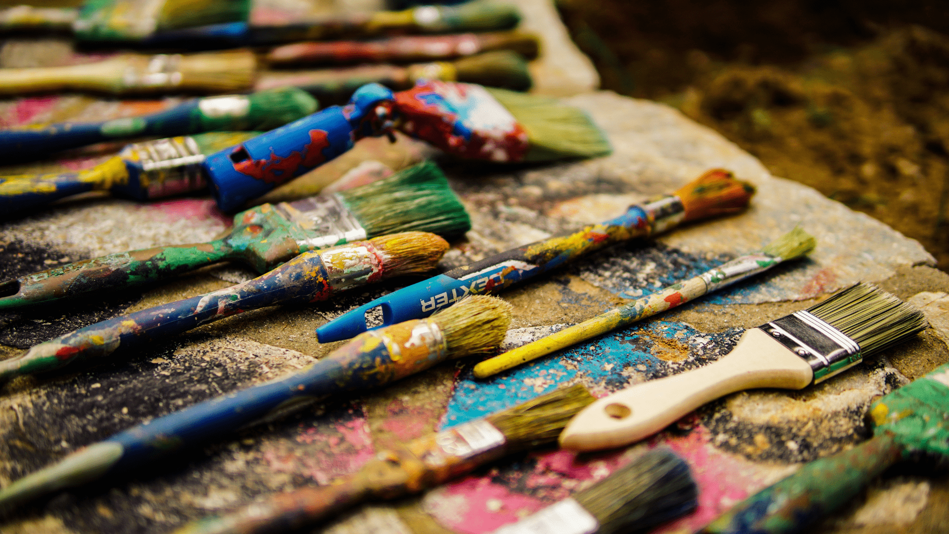 An assortment of heavily used paint brushes lay on a table.