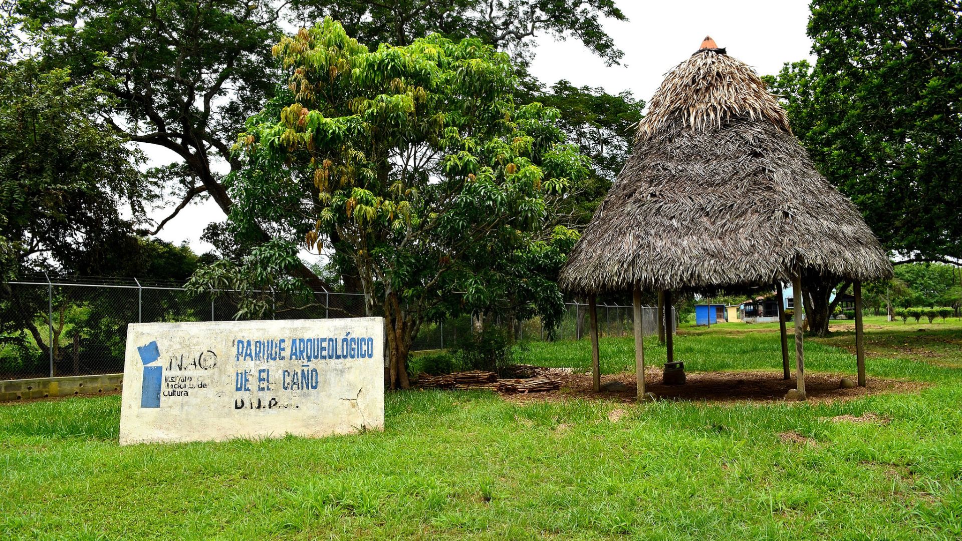 A stone sign and a hut on grass seen at the El Caño Archaeological Park in Panama.