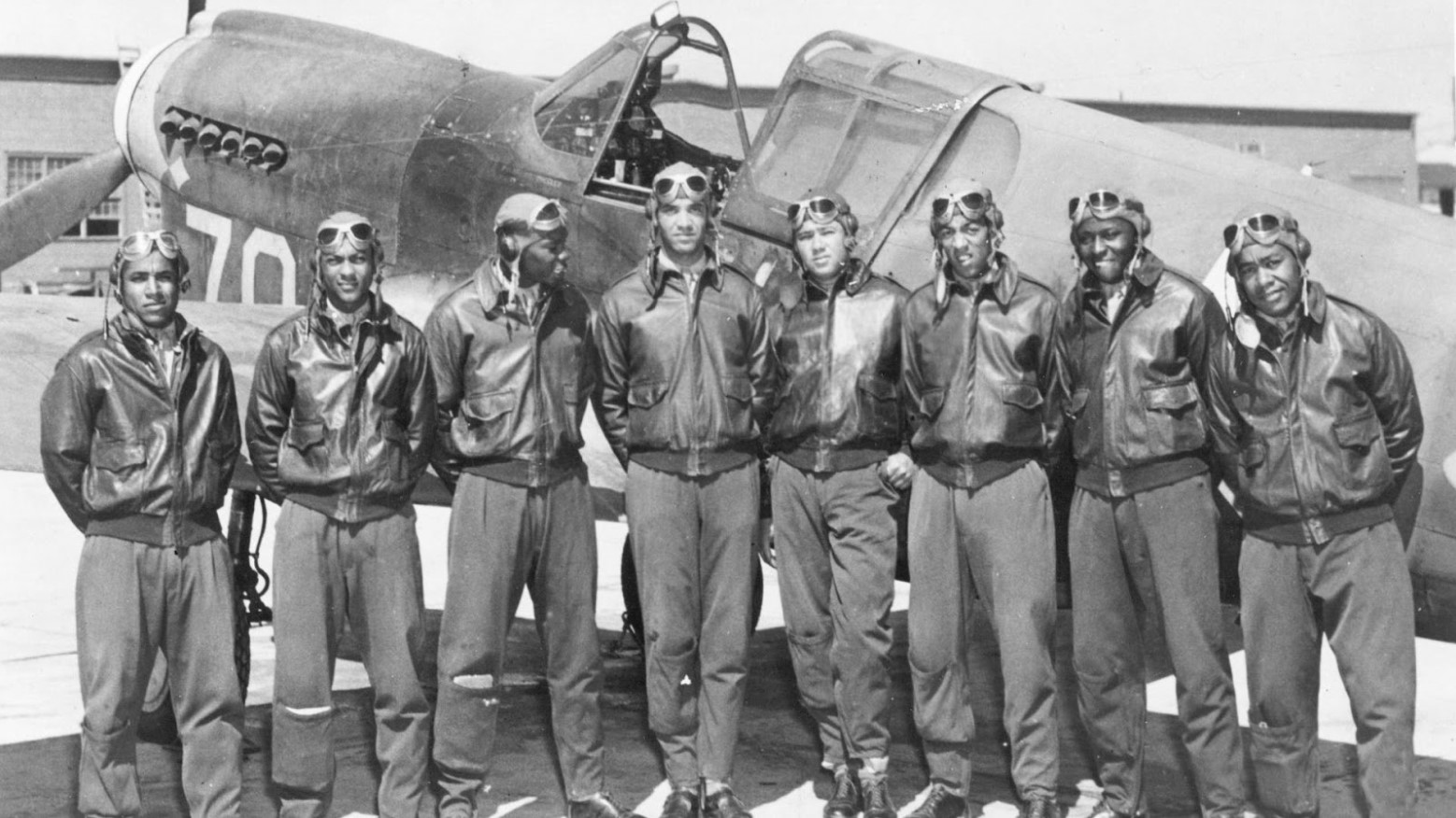 An old black and white photo of the Tuskegee Airmen in front of a plane during World War II.