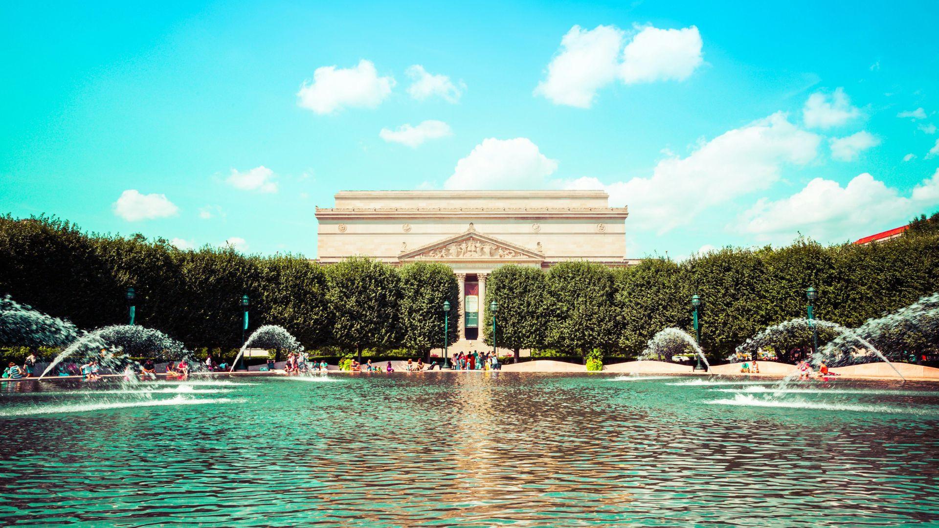 A view of the National Archives and Gallery of Art in D.C. in front of a water fountain in the daytime.