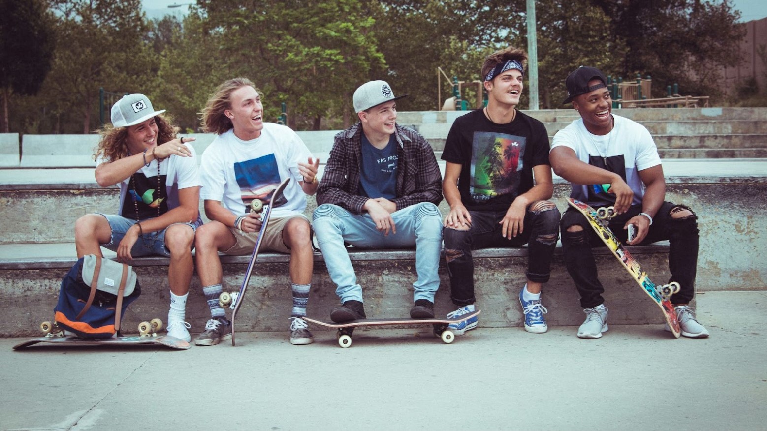 5 young boys sit at a skate park while each holding a skateboard