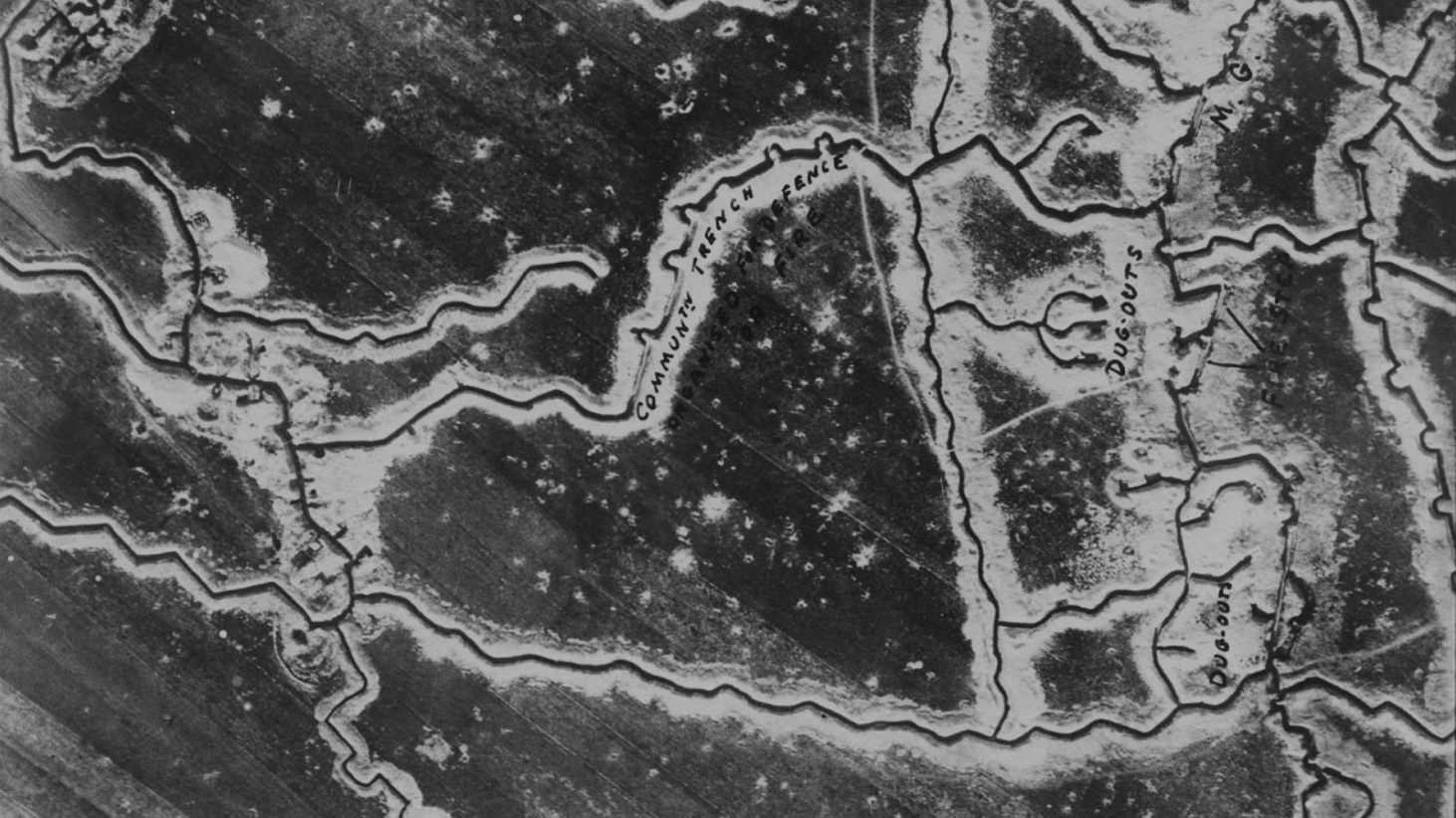 Black and white aerial photograph showing the intricate network of World War I trenches. The zigzagging patterns of the trenches are clearly visible