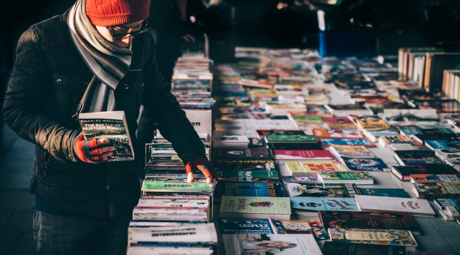 A man looking through some books that are all laid out on a table outside.