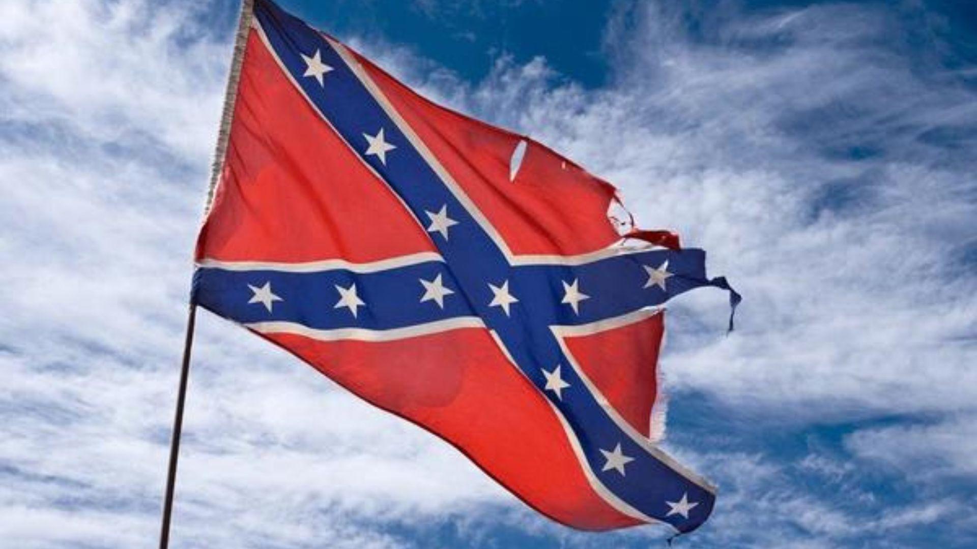 Torn confederate flag flies against a blue sky