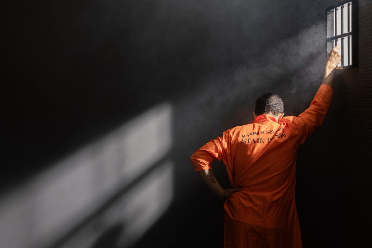 A man is pictured standing with his hand on the wall inside his prison cell