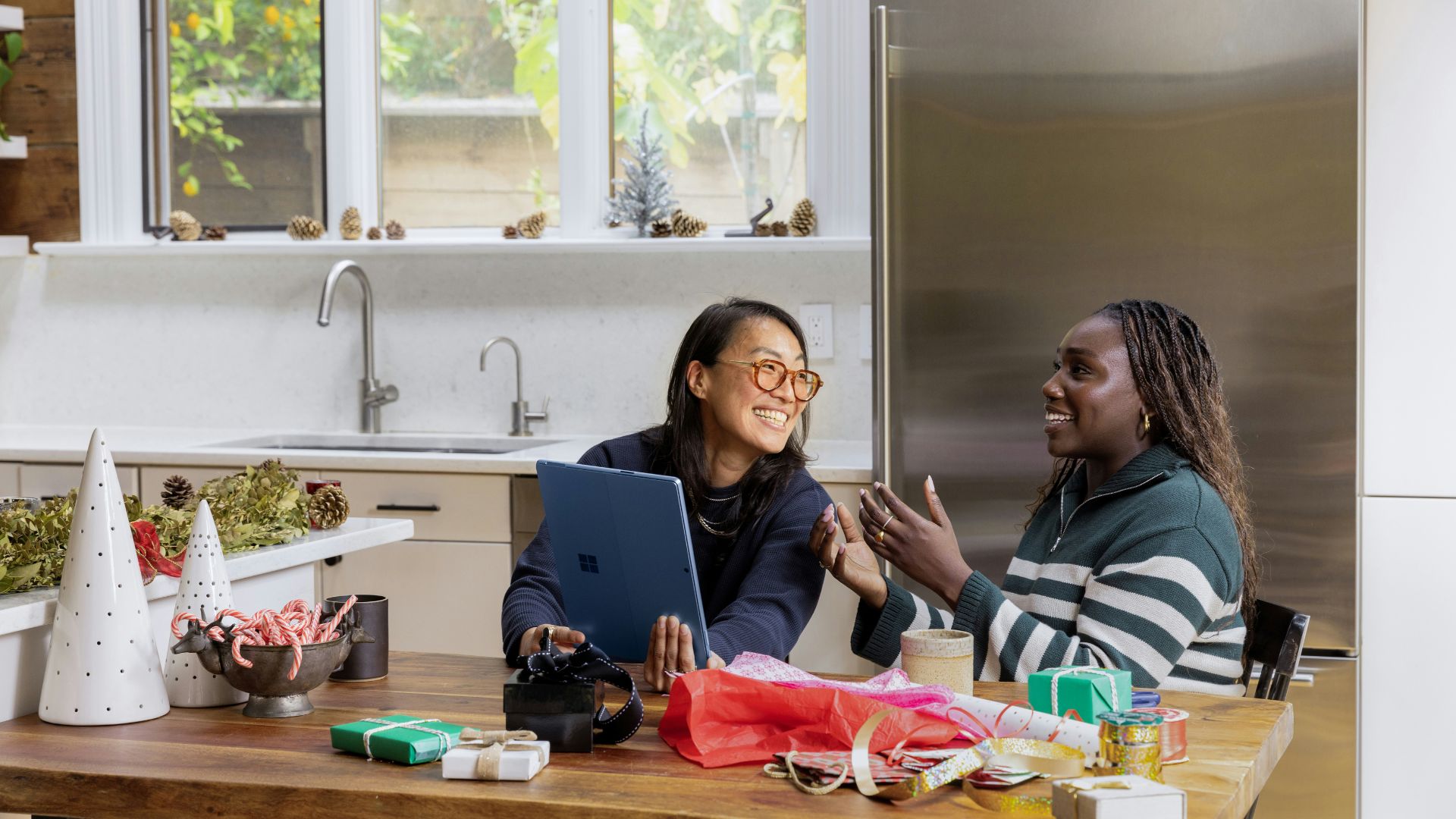 Two people sitting at a table in a kitchen with a tablet smiling and talking.