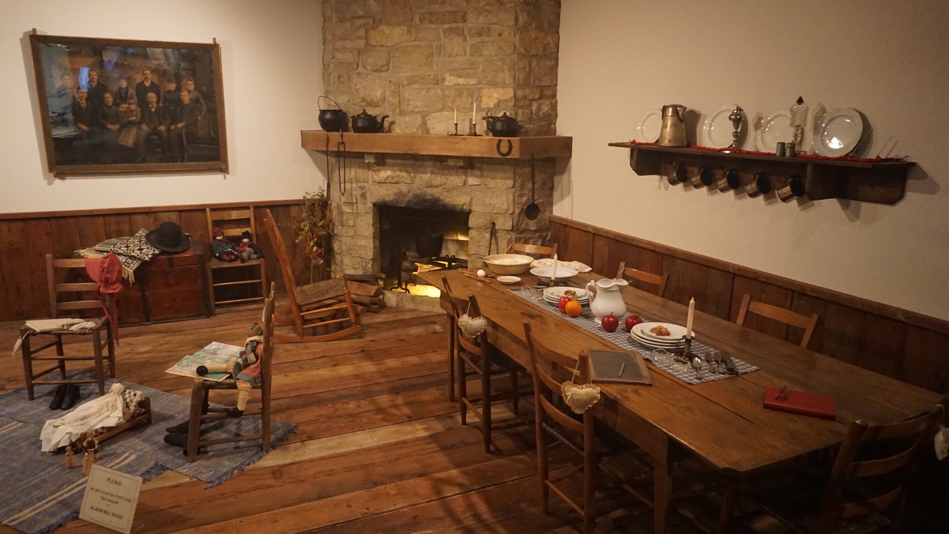 A photo of a frontier life room, with a fireplace and wooden chairs, in a museum.