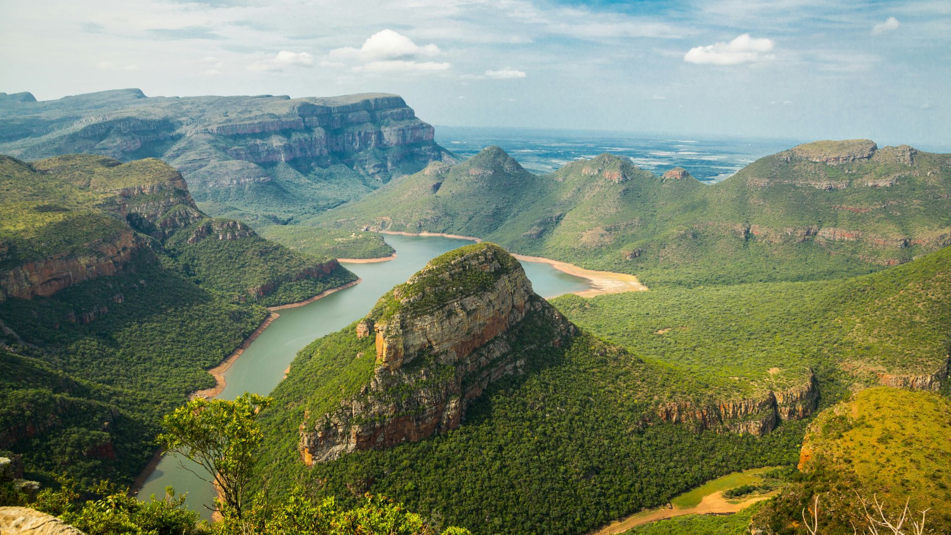 A sweeping landscape view of Blyde River Canyon with its meandering river below, showcasing lush greenery, towering cliffs, and flat-topped mountains