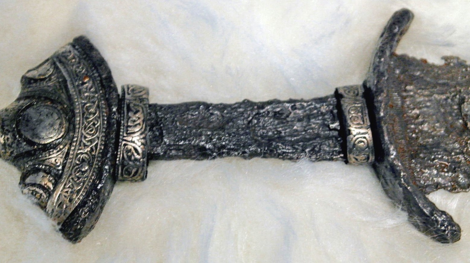 A close-up look at an ancient Viking sword’s pommel against a white background.