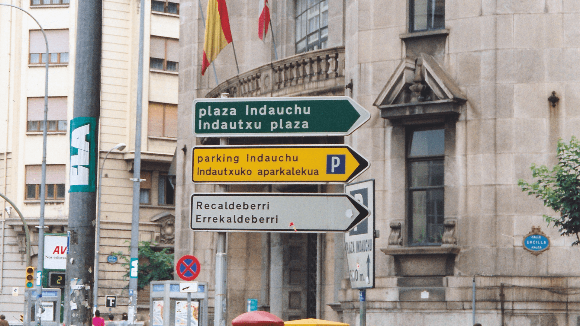 Basque road signs in Bilbao, Spain in 1990. There are three signs, one on top of the other, first in green with white text, then yellow with black text, and finally white with black text.