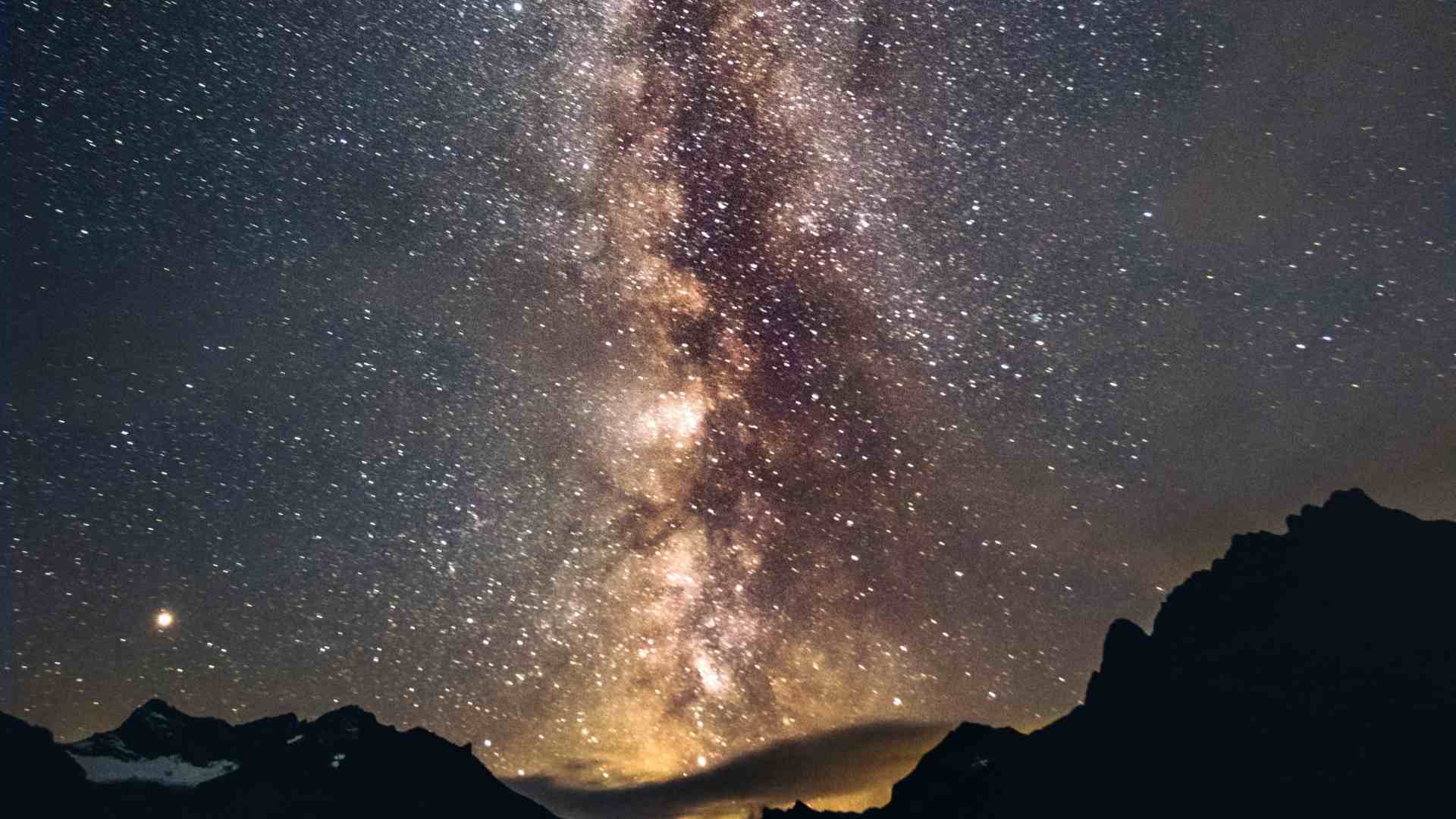 Stars shine brightly in a night sky over mountains.