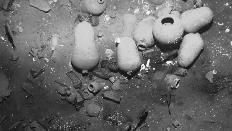 A gray scale underwater image of treasure in the sand from a shipwreck