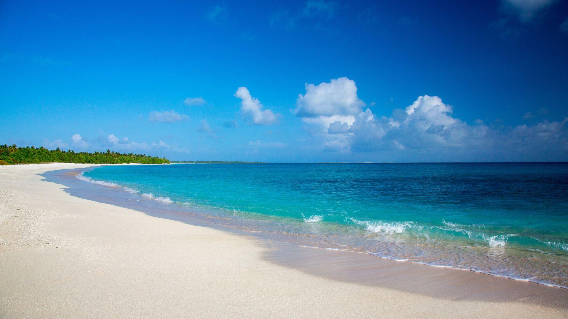 The beach at Bikini Atoll in the Marshall Islands underneath a cloudy blue sky.