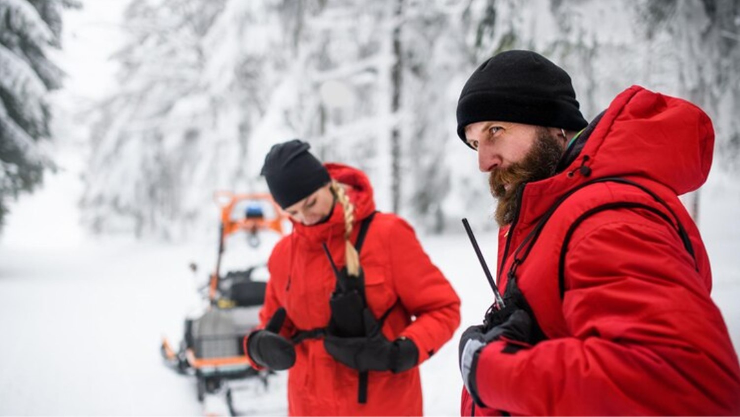 Two people dressed in red coats are pictured as they perform a search and rescue mission in the snow