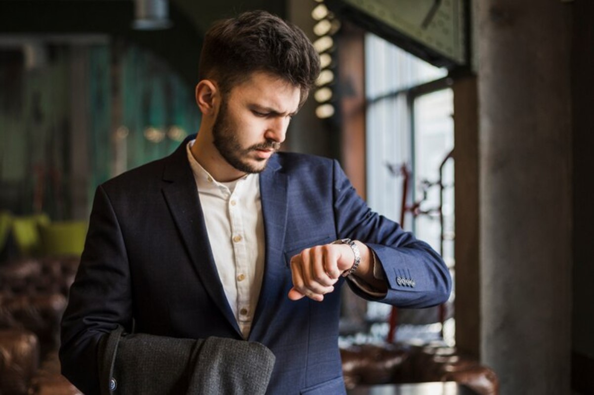 A man dressed in a suit is confused as he checks the time