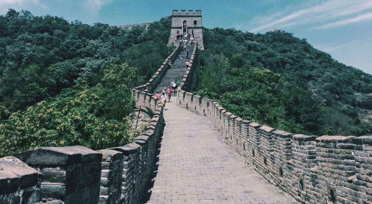 An image from the Great Wall of China, right before some steps leading to a higher part of the wall. People are walking up the steps towards the top of the wall.