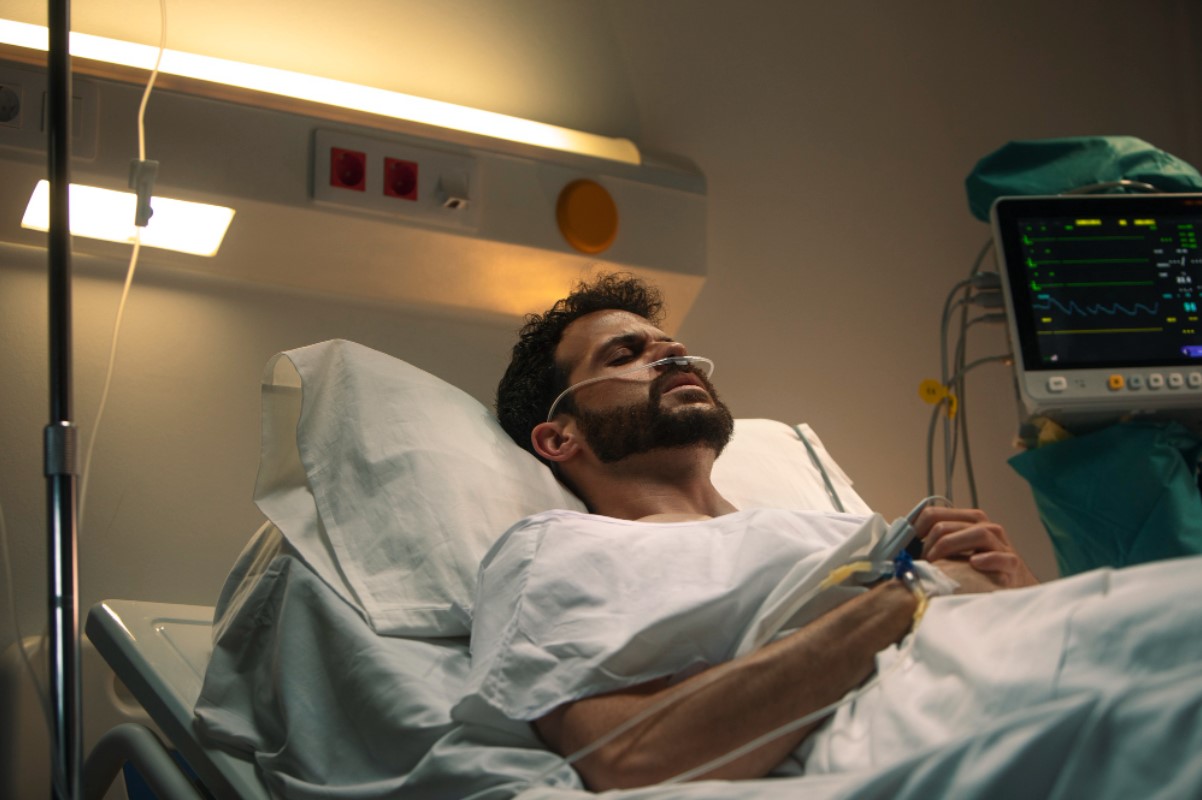 A man pictured in a white gown as he lies in a hospital bed