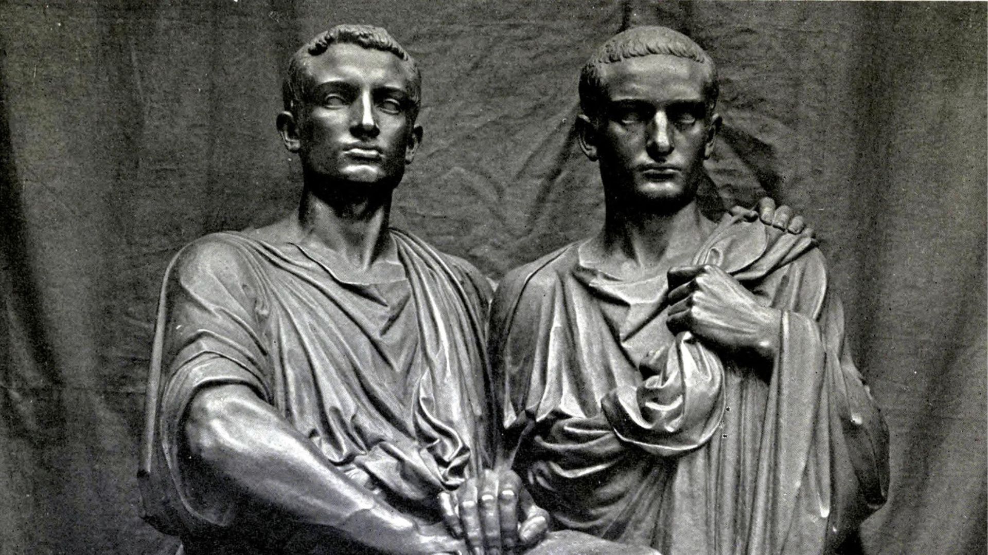 Black and white photo of a stone sculpture depicting two Roman men wearing togas. The figures are the Gracchi brothers and they are standing close together, their bodies angled towards each other, with one hand joined in the center