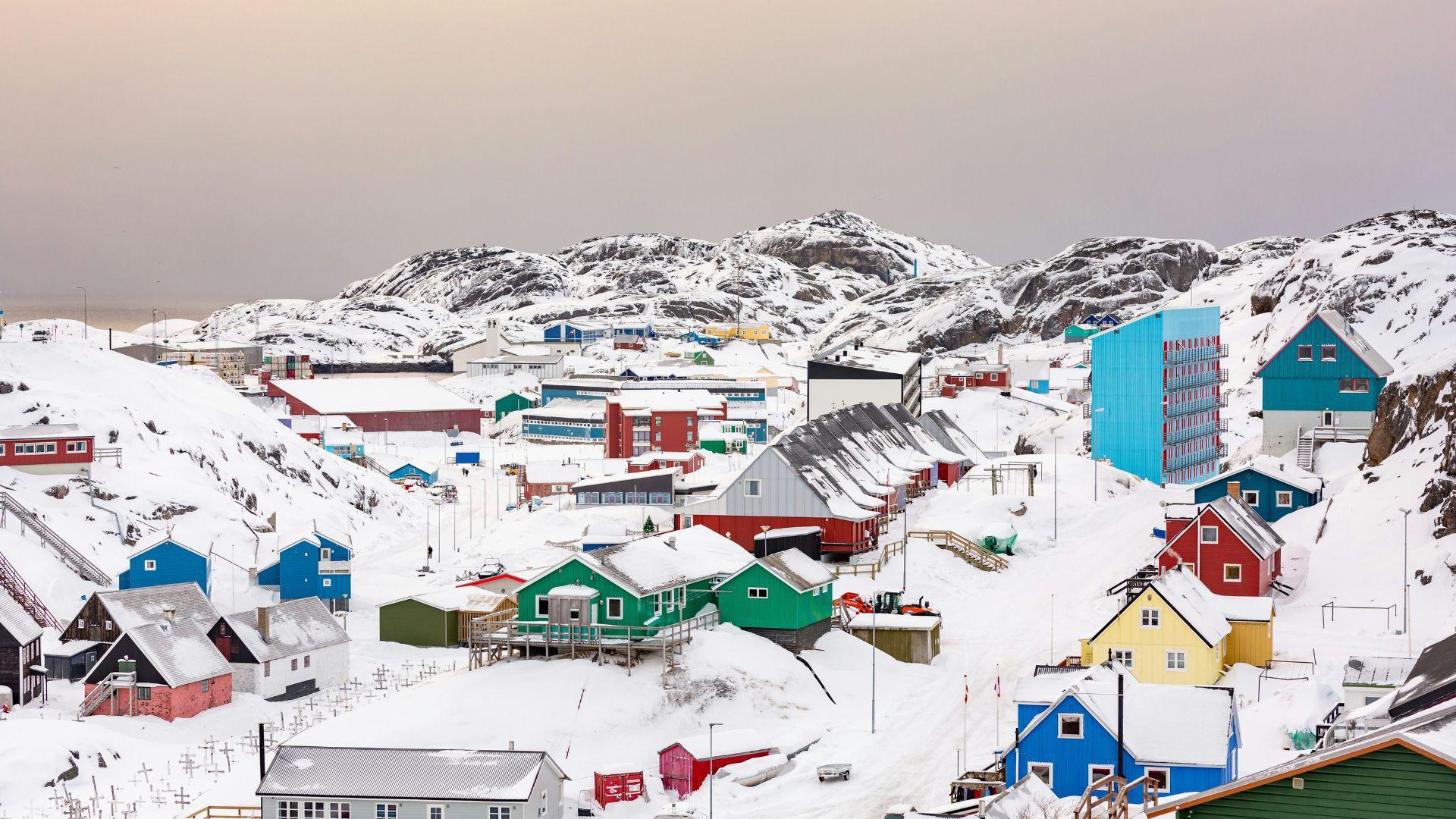 A small town in Greenland, with colorful buildings covered in snow, and snowy mountains in the distance.