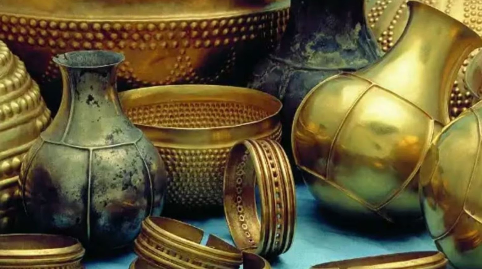 A zoomed-in image of the Treasure of Villena. There are a few gold vases, a gold bowl, and some gold bracelets in the photo.