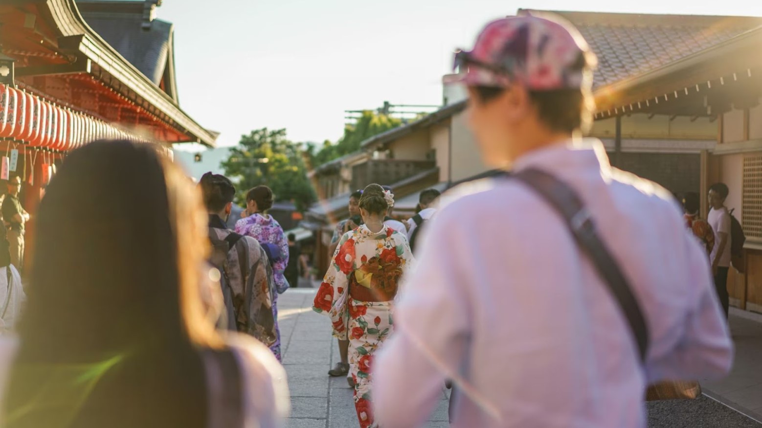 Tourists walking down a street in the geisha district. Some geishas are in front of them wearing floral kimonos.