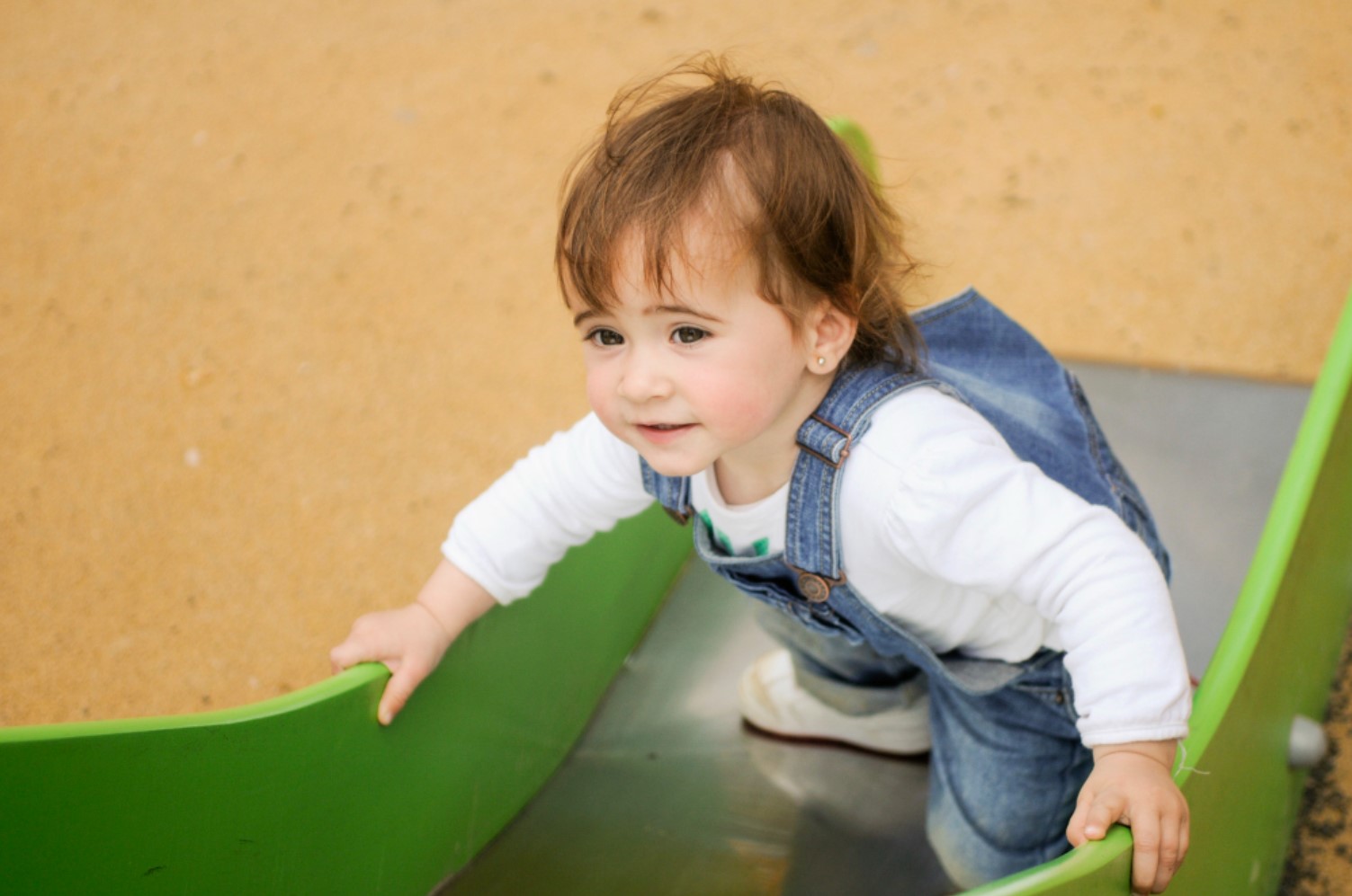 An image of a young child crawling up a slide at a playground