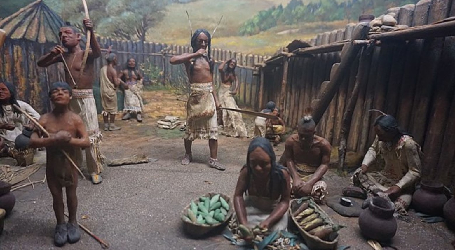 A recreation of an Iroquois tribe in a museum. Some are picking vegetables, and others are doing archery.