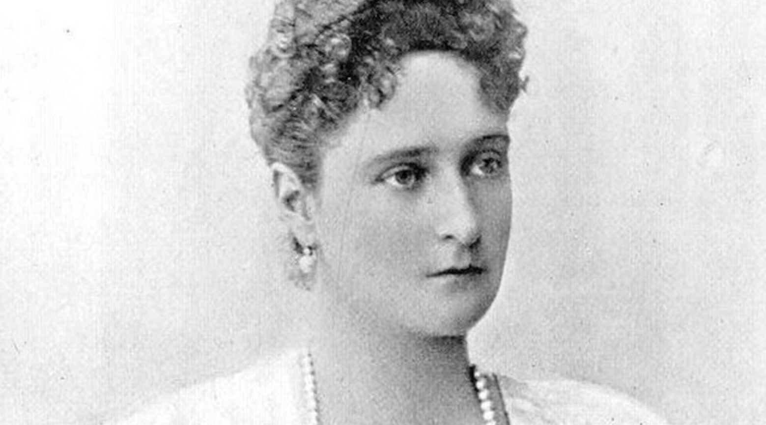 A black and white photo of Czarina Alexandra. Her hair is in curls on top of her hair, and she is wearing matching pearl earrings and necklace.