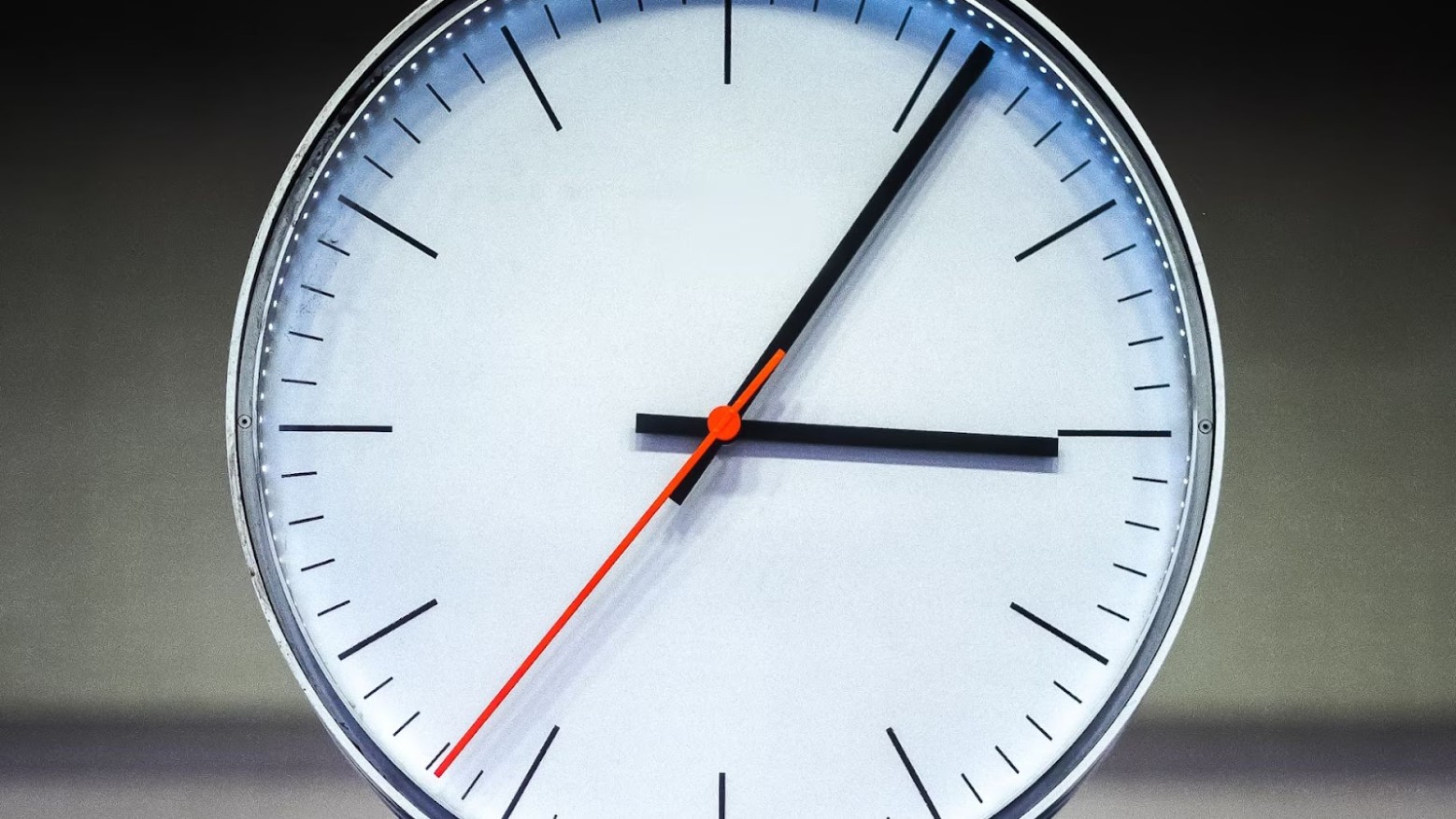 A white analog clock with a red second hand and black hour and minute hands. The clock is at 3:05.
