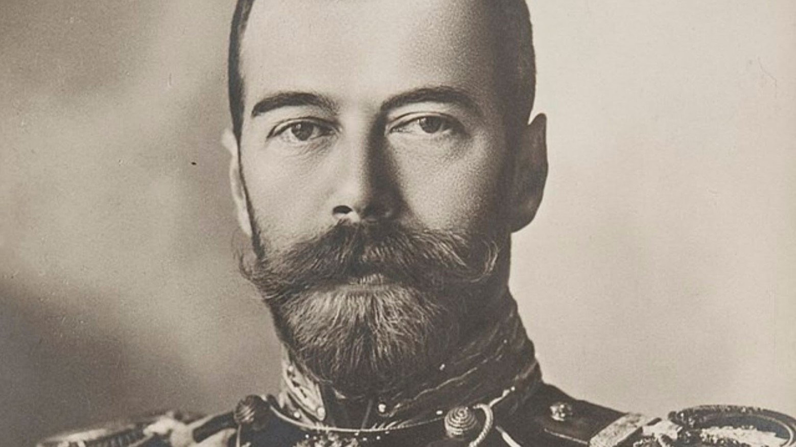This is a black-and-white portrait of Czar Nicholas II. He has a thick beard and mustache and is wearing an army uniform.
