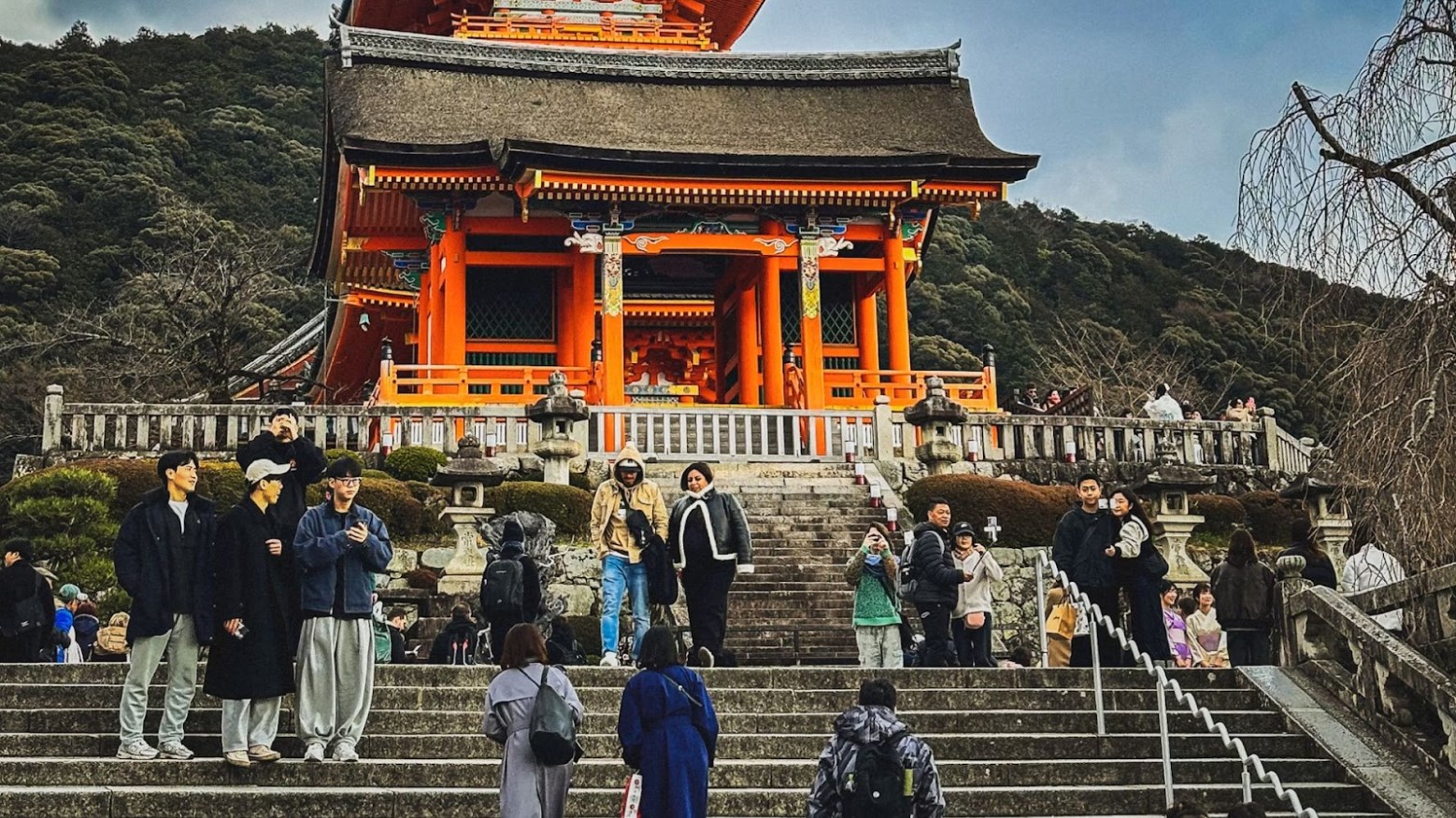 Tourists in Japan. They are in groups standing on some steps in front of an orange building