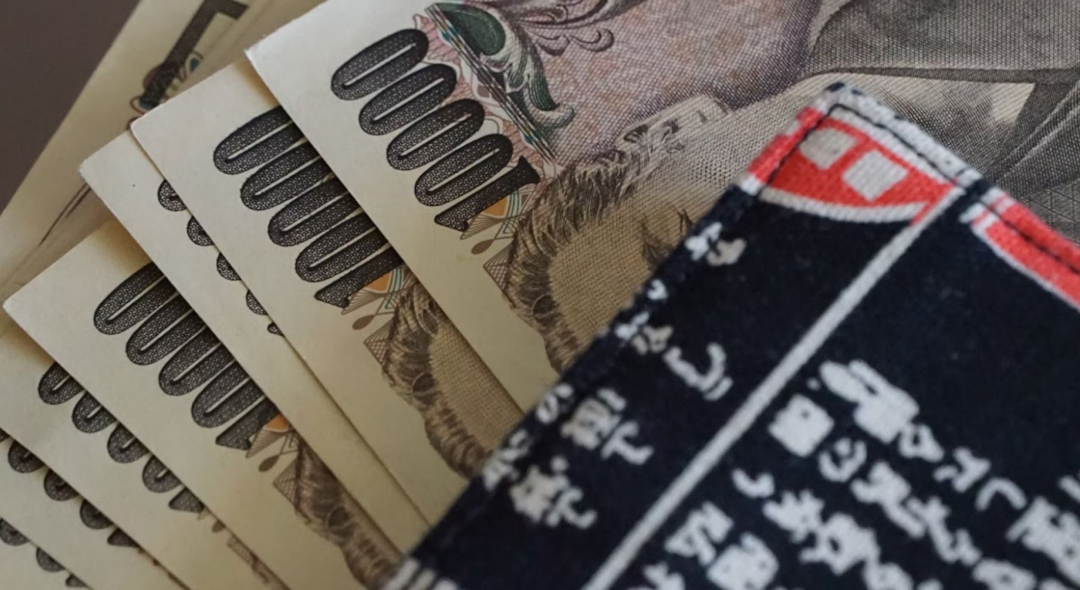 A black, white, and red wallet on a table on top of some fanned-out 10,000 Yen notes.