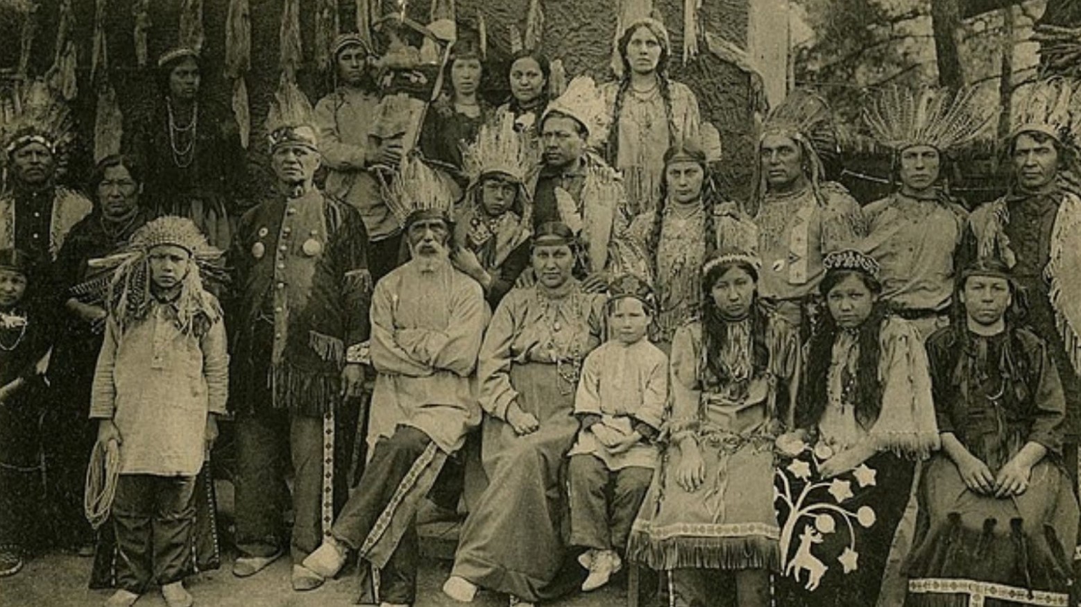 This is a black-and-white photo of an Iroquois tribe. The men, women, and children are all wearing Native American headdresses.