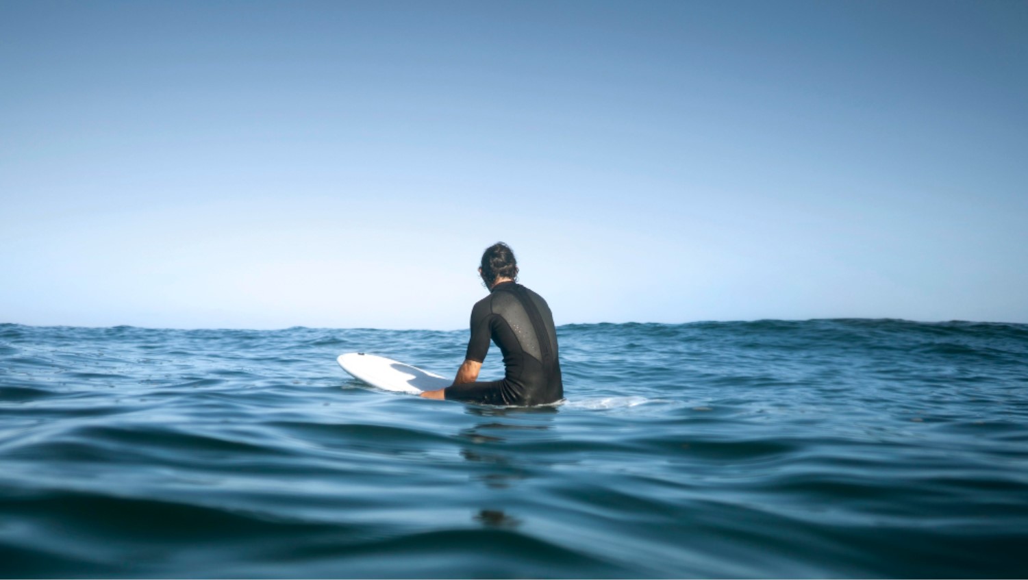 An image of a surfer as he looks out to the ocean's horizon