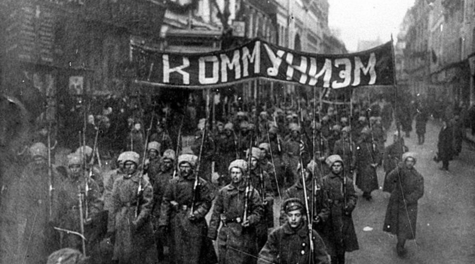 This is a black-and-white image of a protest in Russia in 1917 during the Russian Revolution. Protestors are holding up a sign in Russian that reads “Communism.”