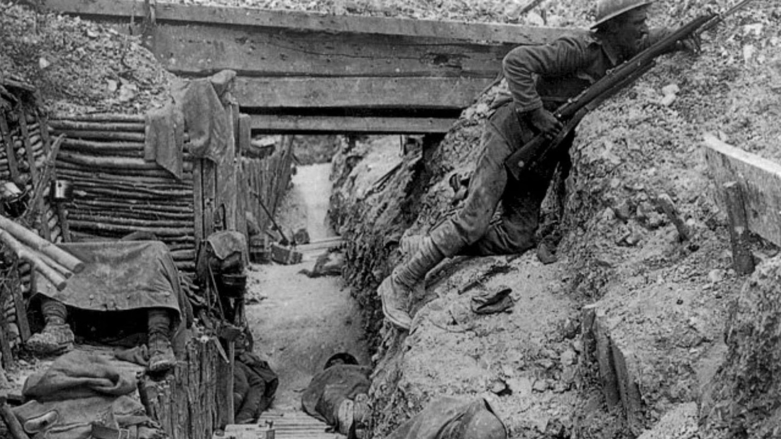 This is a black-and-white image from World War I. It shows one of the trenches with a soldier hiding in the trenches holding a gun.