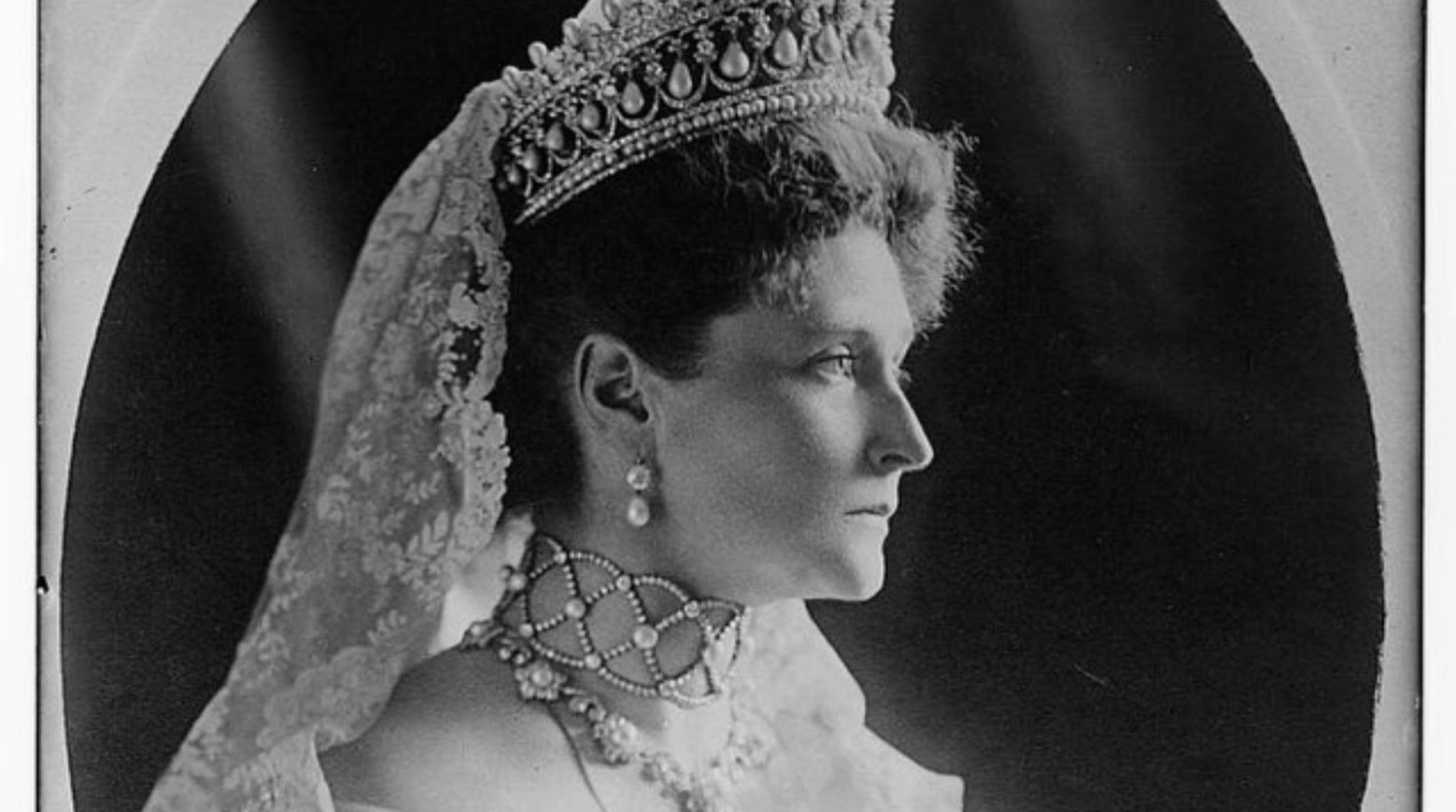 A portrait of Czarina Alexamdra. She is wearing a lace veil attached to a tiara, pearl earrings, and a pearl necklace.