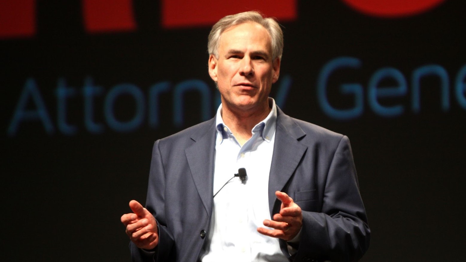 Greg Abbott in a suit speaking with his hands slightly raised.