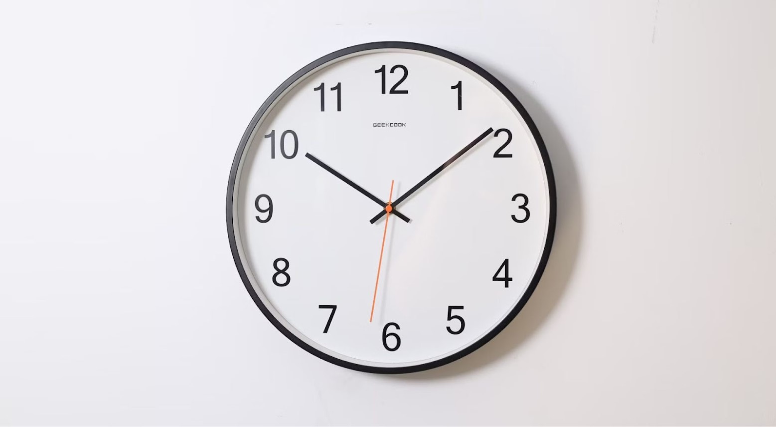 A white and black analog clock against a white wall. The second hand is red and the hour and minute hands are black. The time is 10:10.