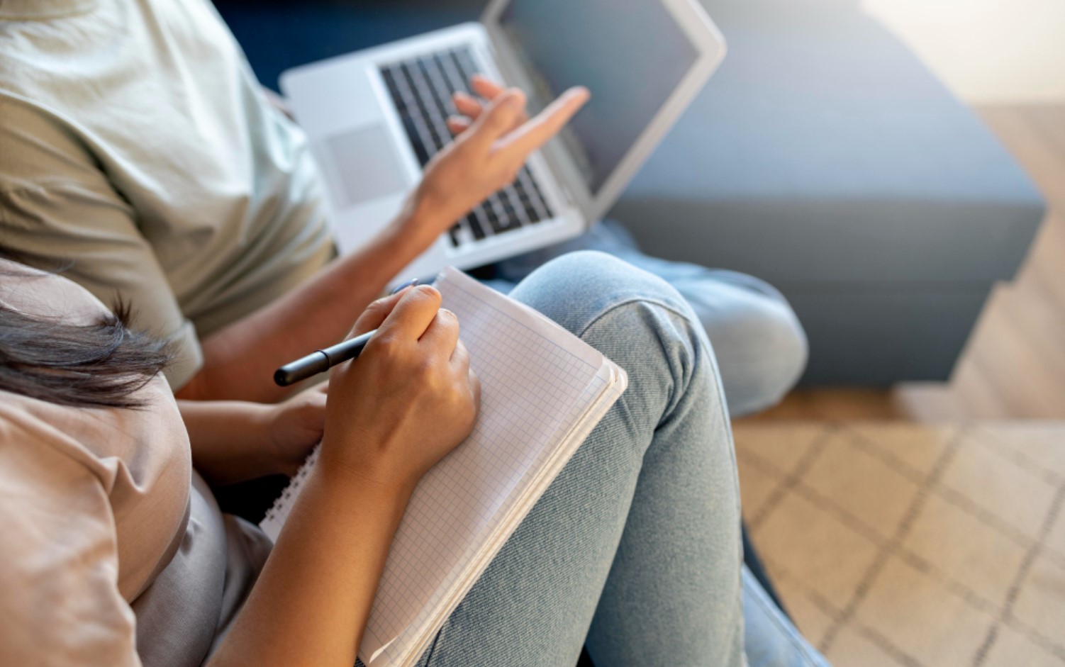 An image of a woman writing down notes as her friends search for information online